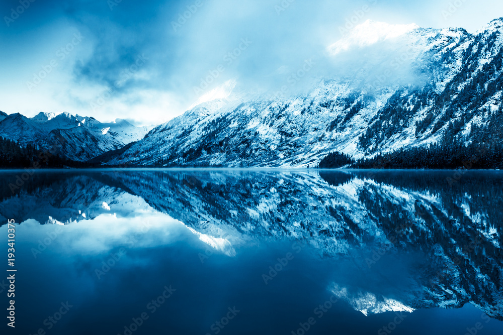 Beautiful blue lake in the mountains. Flat mirror surface of the water under the clouds. The beauty of winter nature. A tourist Trip through the nature reserve of Altai.
