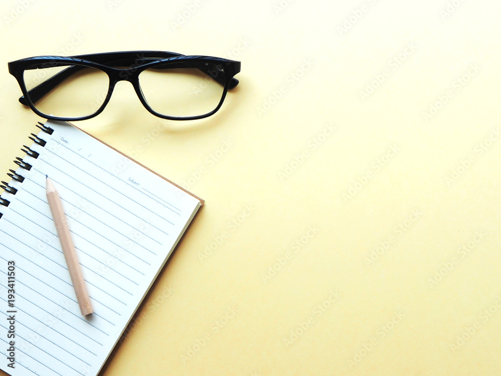 Soft focus blank small notebook with small brown pencil and black glasses on a light yellow table, business planning concept, minimalist Soft focus blank small notebook with small brown pencil and black glasses on a light yellow table, business planning concept, minimalist