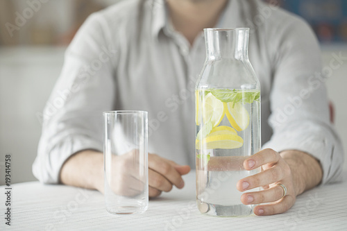 Young man having bottle of water and glass in kitchen