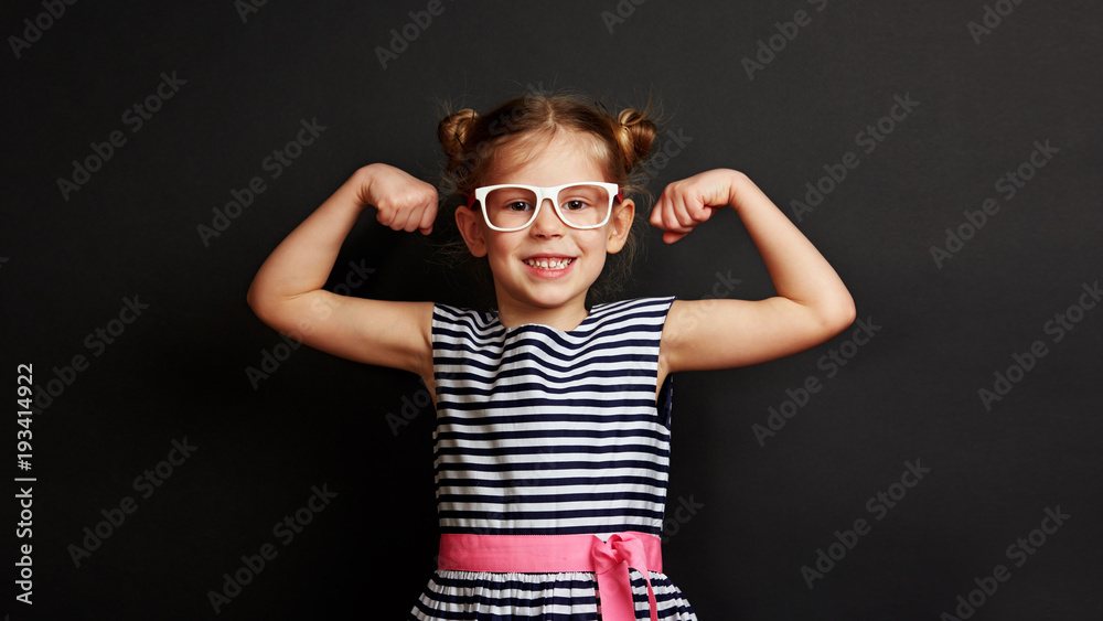 Pretty smiling child showing biceps muscles over dark background. Concept of power and success. Pretty smiling child showing biceps muscles over dark background. Concept of power and success.