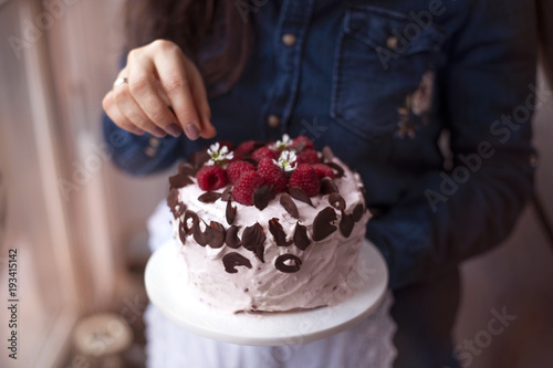A woman is holding a beautiful cake with pink cream and fresh raspberry berries, decorated with chocolate. Calorie food. Free space for text or postcard.