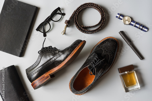 Top view of men leather shoes and accesories in black tone, wingtip shoes on grey background
