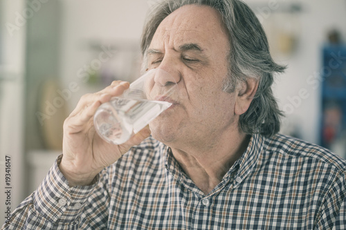 Senior man drinking water from glass in kitchen