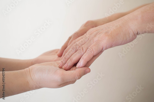 National Family Caregiver Month. Close up of young female caregiver hand holding senior hand. Health care for elderly person, Parkinson's disease, Alzheimer's disease, dementia and disability person.