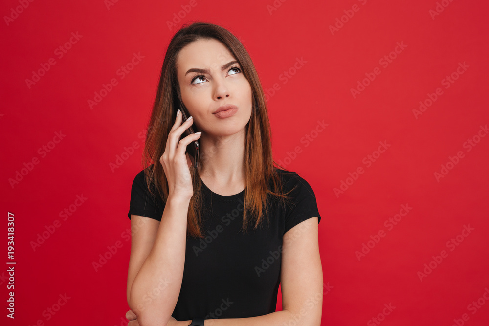 Photo of irritated woman in black clothing looking upward while fed up with mobile talking of interlocutor, over red background Photo of irritated woman in black clothing looking upward while fed up with mobile talking of interlocutor, over red background
