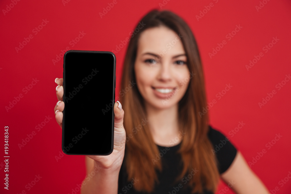 Caucasian woman with long brown hair doing commercial and presenting new mobile device in focus on camera, isolated over red background Caucasian woman with long brown hair doing commercial and presenting new mobile device in focus on camera, isolated over red background