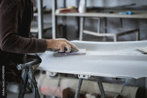 Fotografie Car detailing - Man with sandpaper in auto repair shop sanding polishing and preparing car parts for painting
