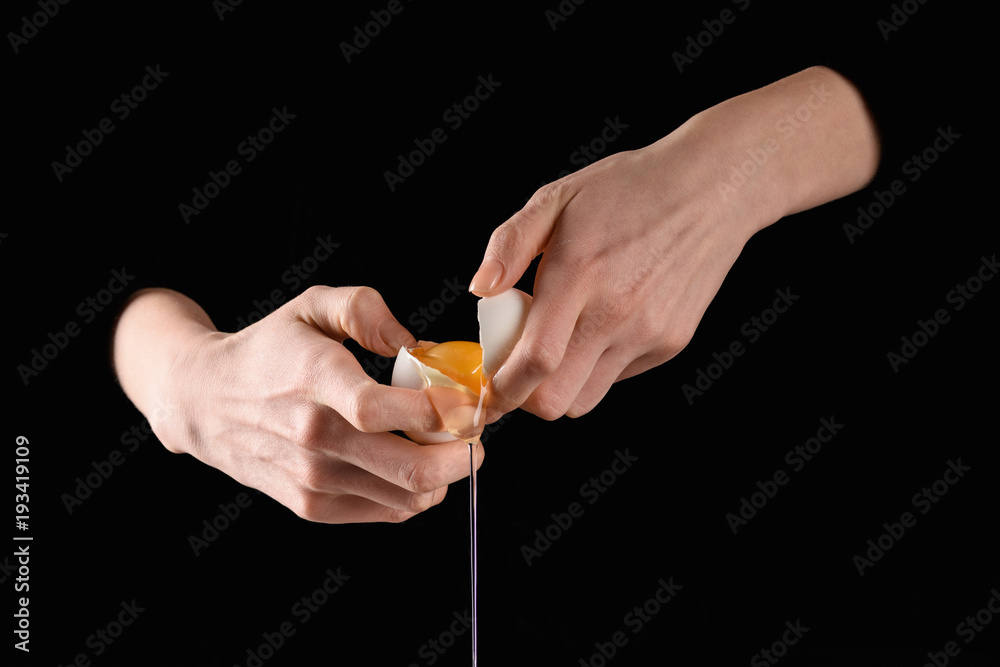 cropped image of woman holding broken dripping chicken egg in hands isolated on black cropped image of woman holding broken dripping chicken egg in hands isolated on black