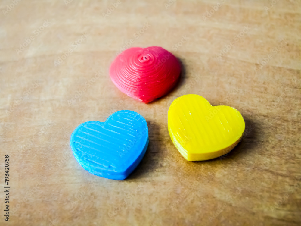 Fototapeta premium Three hearts on wooden background. Photo of 3d-printed objects.