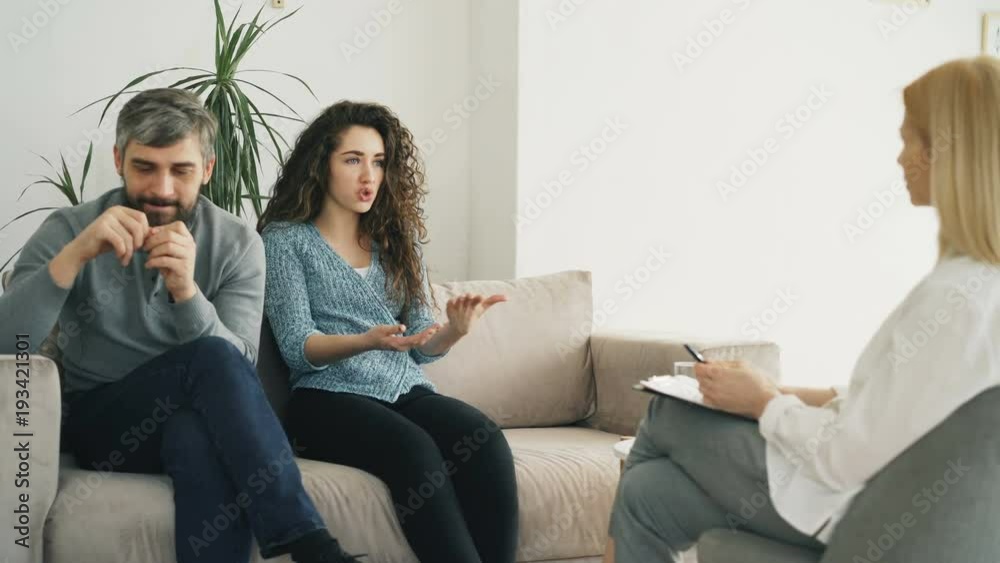 Angry woman arguing and talking about her husband to marriage counselor. Young couple visiting professional psychologist office Angry woman arguing and talking about her husband to marriage counselor. Young couple visiting professional psychologist office