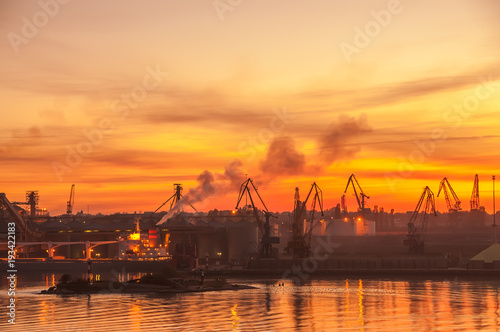 View of the port at sunset. Industrial warehouse complex on the shore of the bay. Silhouettes of the cranes in the sunset. 