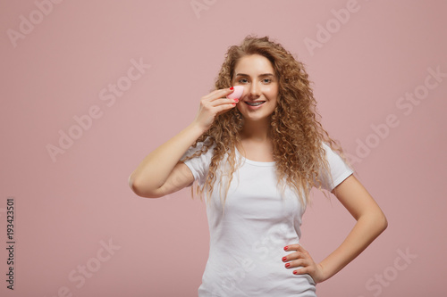 Beauty blender. Beautiful girl with curly hair with makeup sponge in hands looking into camera. Concept of doing make-up on your own home