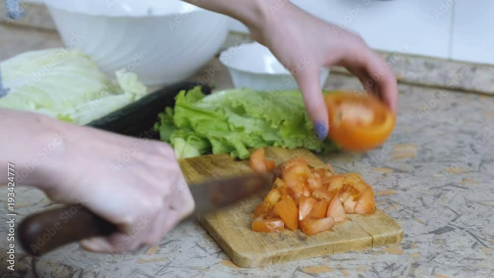 Unrecognizable woman cut tomato into small pieces on cutting board on kitchen table. Hands close up. Unrecognizable woman cut tomato into small pieces on cutting board on kitchen table. Hands close up.