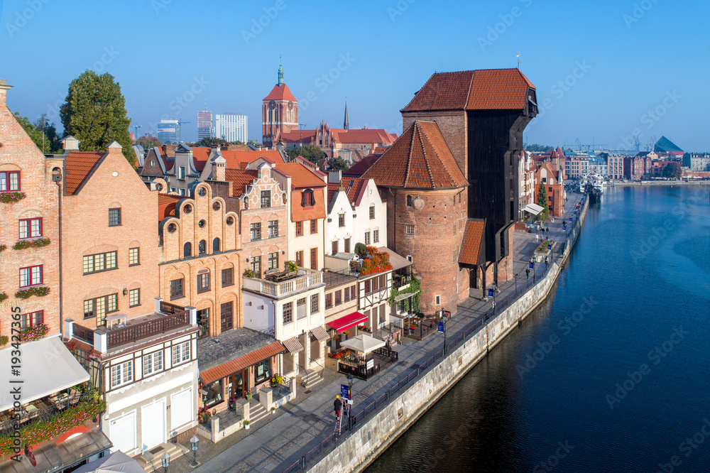 Obraz premium Gdansk old city in Poland with the oldest medieval port crane (Zuraw) in Europe, St John church and Motlawa River with embankment and promenade. Aerial view in early morning. Sunrise light.