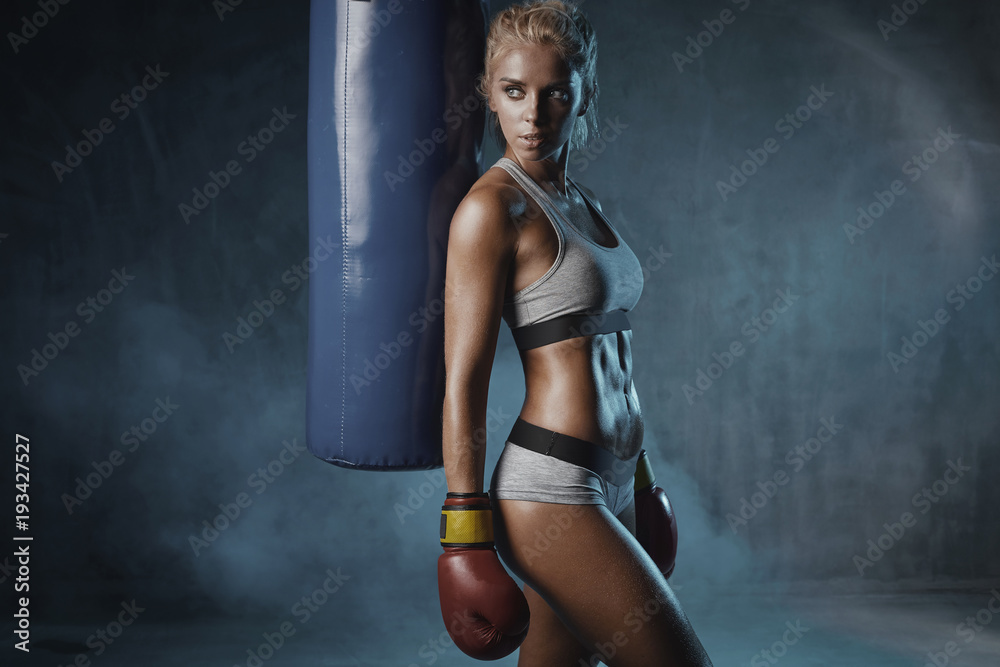 Portrait of sexy hot blonde boxer woman in red boxing gloves and grey sports  bra and panties standing near blue punching bag Photos | Adobe Stock