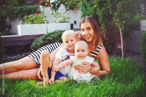 woman mother with two young children lie on a green lawn, concept maternity and parenting © lanarusfoto