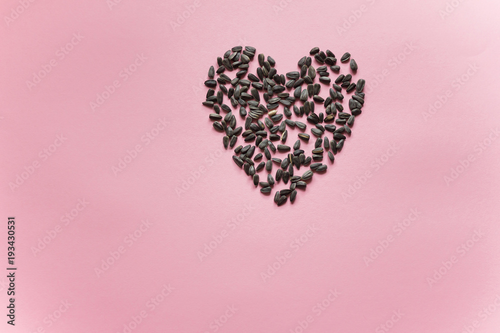 Heart laid out from black sunflower seeds on a purple background close up