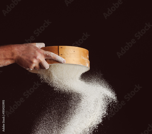 men's hands are sifting flour through a sieve on black background photo