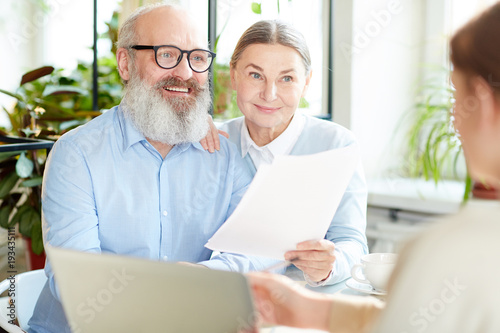 Happy modern senior couple with papers having talk to insurance agent in cafe