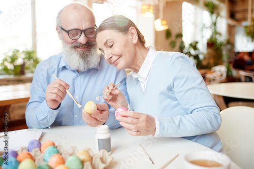 Photography Aged couple with eggs and paintbrushes sitting by table and sharing creative ide