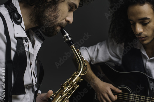 duet of jazzmen playing sax and acoustic guitar on black
