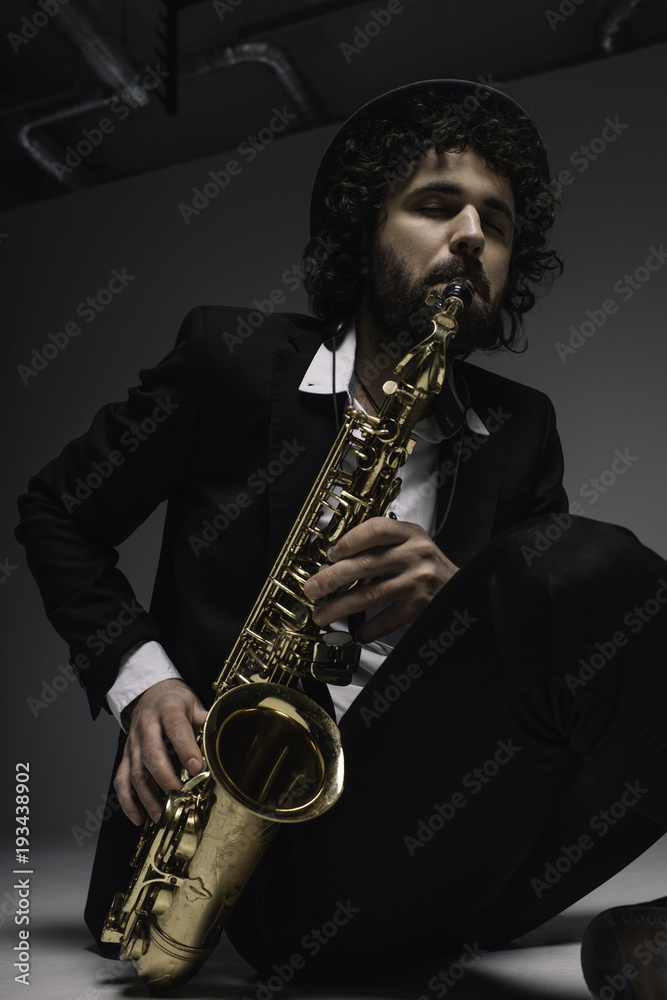 Fototapeta premium artistic musician playing saxophone while sitting on floor