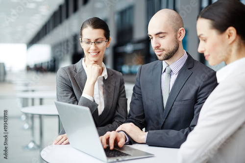 Confident business partners in formalwear sitting by table in airport lounge and browsing in the net