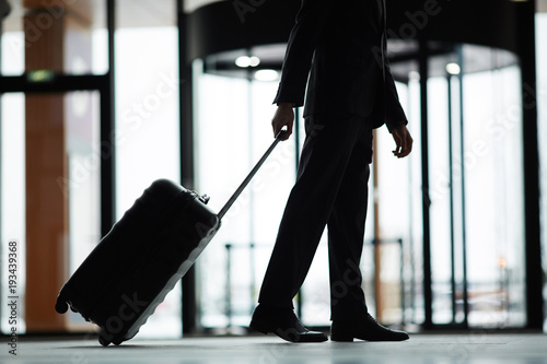 Silhouette of lowsection of business traveler with suitcase moving down modern airport photo