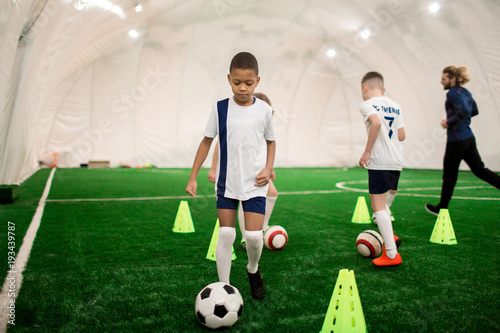 Young boys running throughout football field and training with ball around soccer pylons