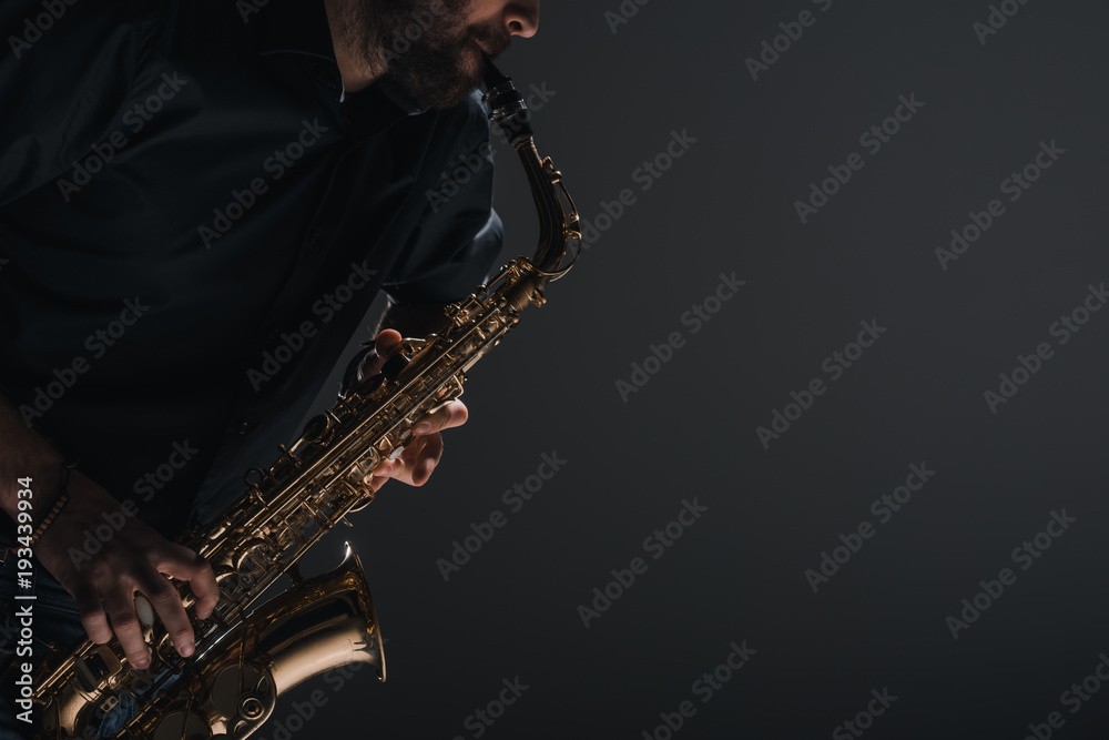 Naklejka premium cropped shot of jazzman playing saxophone on black