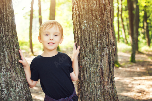 Happy cute boy leaning against tree and smiling during walking in a forest.