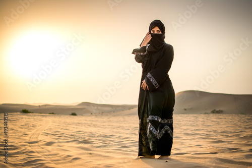 Full length portrait of Arab woman in burka clothing standing in the desert. photo