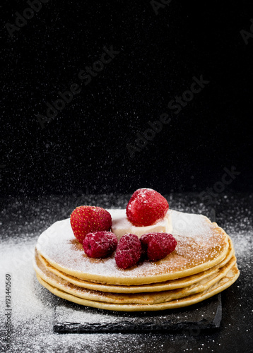 Pancakes with berries and sugar on dark background
