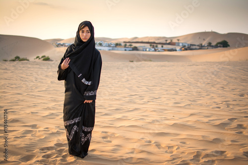 Cuadro en lienzo Full length portrait of Arabic woman in traditional black clothes standing in the desert in front of Bedouin village