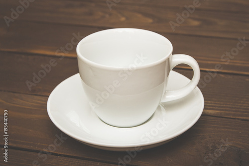 Empty white Cup with saucer on a wooden background , special toning . Crockery for coffee and tea . Template for advertising and multimedia.