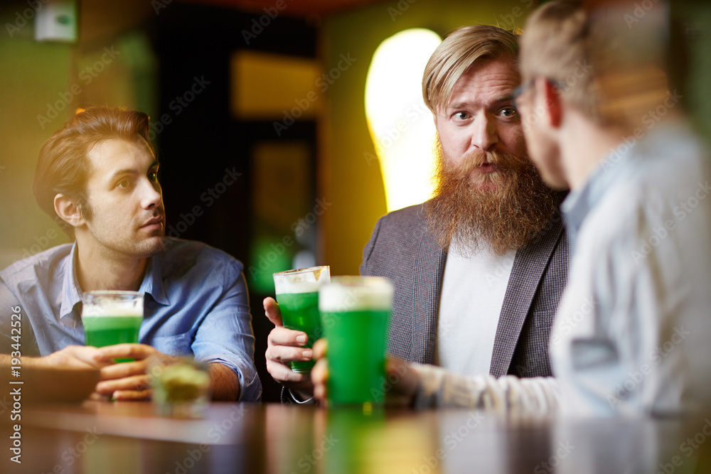 Three friendly men sitting by table or bar counter in pub and having beer Three friendly men sitting by table or bar counter in pub and having beer