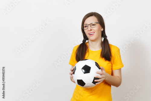 European young sad upset woman, two fun pony tails, football fan or player in glasses, yellow uniform hold classic soccer ball isolated on white background. Sport, play, football, healthy lifestyle © ViDi Studio
