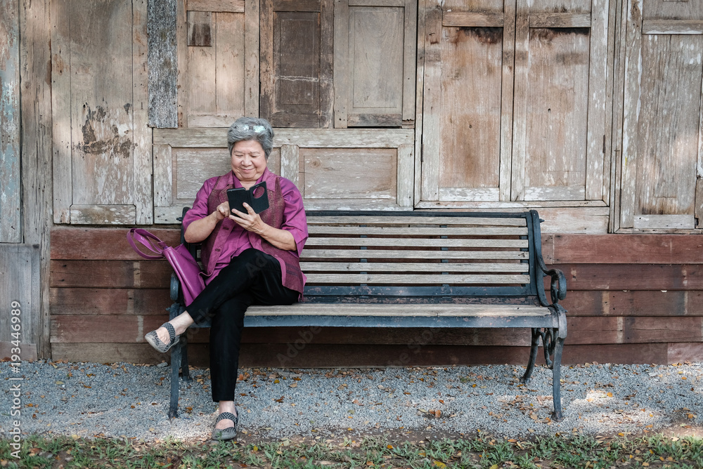 elder woman holding mobile phone in garden. elderly female texting message, using app with smartphone in park. senior use cellphone to connect with social network