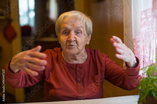 An elderly woman talks emotionally sitting at the table.
