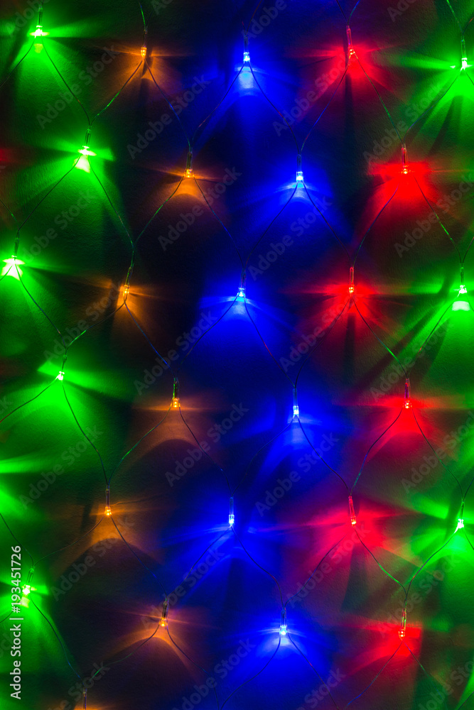 Background image of varicolored lights of a garland in a row on the wall closeup
Background image of varicolored lights of a garland in a row on the wall closeup