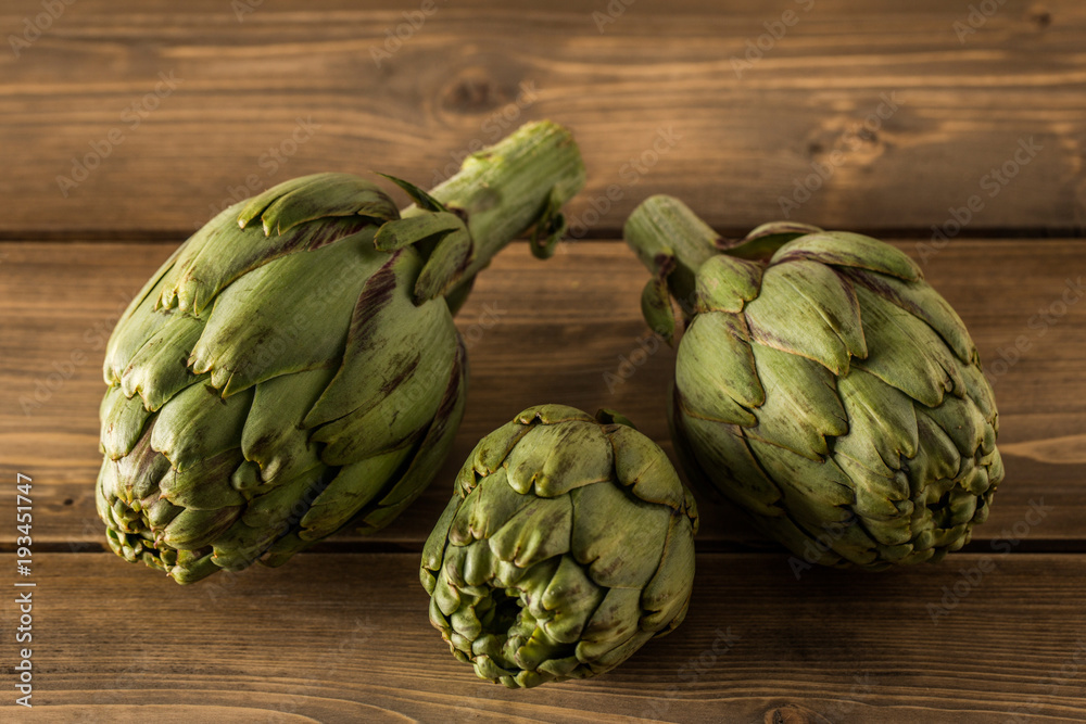 Fototapeta premium Natural artichokes on a rustic wooden table.
