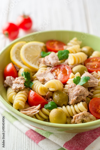 Fusilli pasta salad with tuna, tomatoes, olives and parsley on white wooden background.