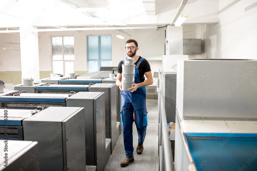 Typographer carrying paint buckets walking on the offset machine at the printing manufacturing Typographer carrying paint buckets walking on the offset machine at the printing manufacturing