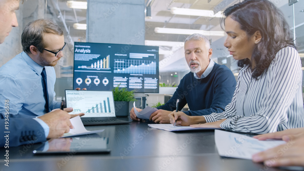 Diverse Group of Successful Business People in the Conference Room, Work on a Company's Growth, Share Charts and Statistics. In the Background Wall TV with Corporate Data on it. Diverse Group of Successful Business People in the Conference Room, Work on a Company's Growth, Share Charts and Statistics. In the Background Wall TV with Corporate Data on it.