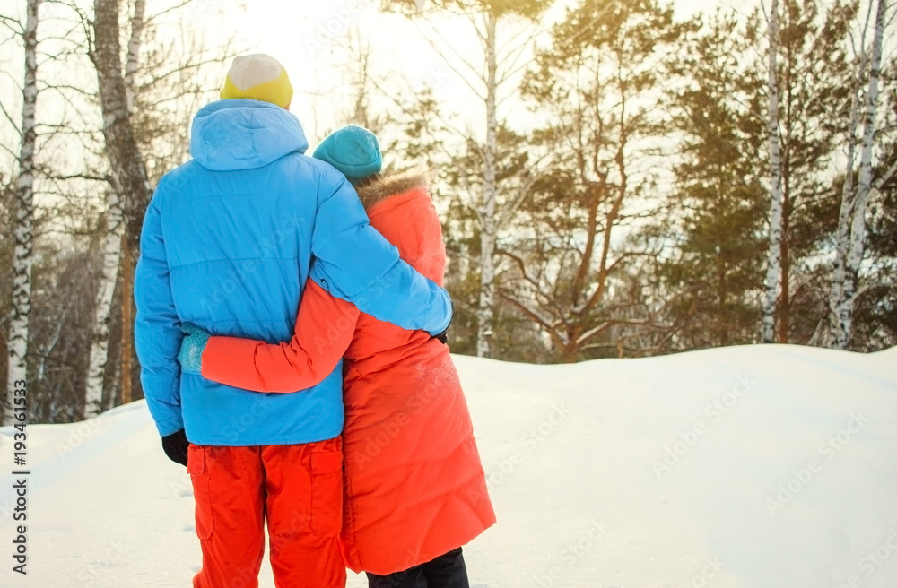 Young couple in winter snowy park or forest. Man hug his girlfriend and both of them are standing and looking to sunset from mountain. Valentine's day. Young couple in winter snowy park or forest. Man hug his girlfriend and both of them are standing and looking to sunset from mountain. Valentine's day.