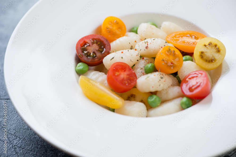 Closeup of boiled potato gnocchi served with fresh sliced tomatoes and green peas in a white plate, selective focus Closeup of boiled potato gnocchi served with fresh sliced tomatoes and green peas in a white plate, selective focus