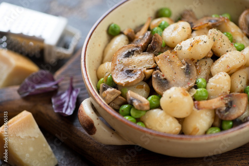 Bowl of potato gnocchi with fried champignons and green peas, close-up, selective focus, studio shot