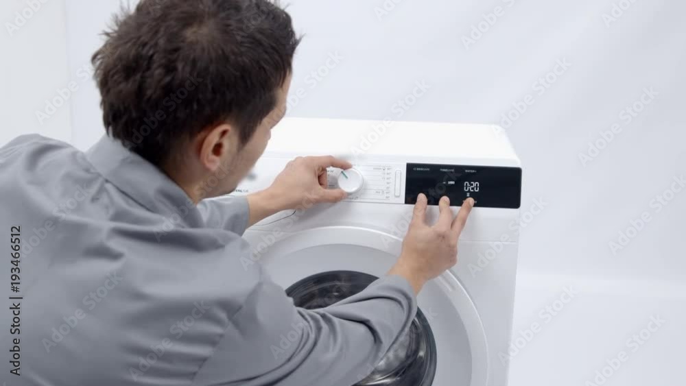 A repairman is checking something on the touch screen of the washing machine. He is looking if the device is now working properly. A repairman is checking something on the touch screen of the washing machine. He is looking if the device is now working properly.