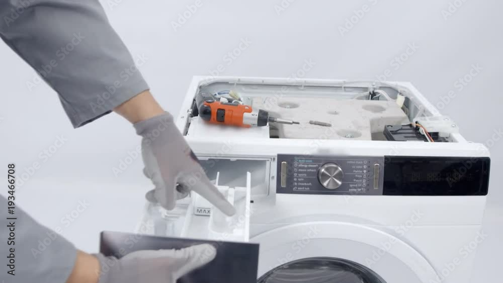 A repairman is taking out a dispenser from a washing machiner. He will dismantle the device because he needs to fix something. A repairman is taking out a dispenser from a washing machiner. He will dismantle the device because he needs to fix something.