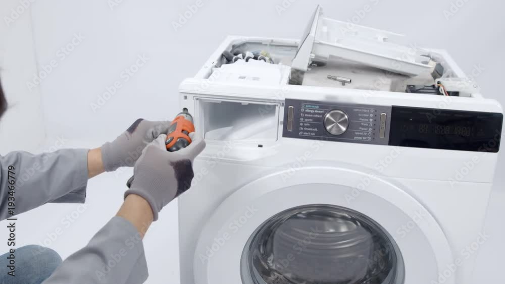A repairman is dismantling a washing machine and he is taking out screws. He needs to fix the device. A repairman is dismantling a washing machine and he is taking out screws. He needs to fix the device.